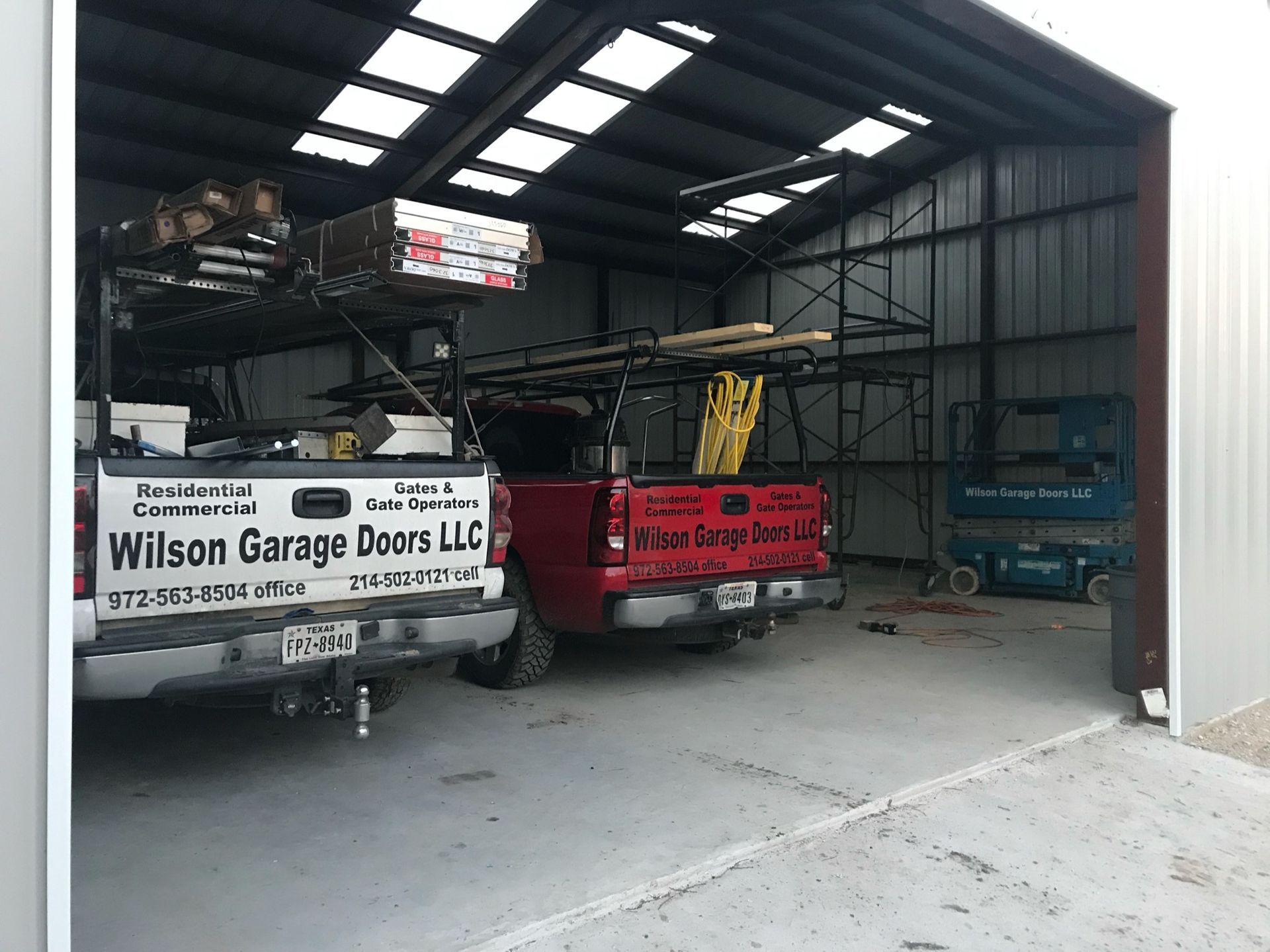 Two red trucks are parked in a garage with a sign on the back that says wilson garage doors llc.