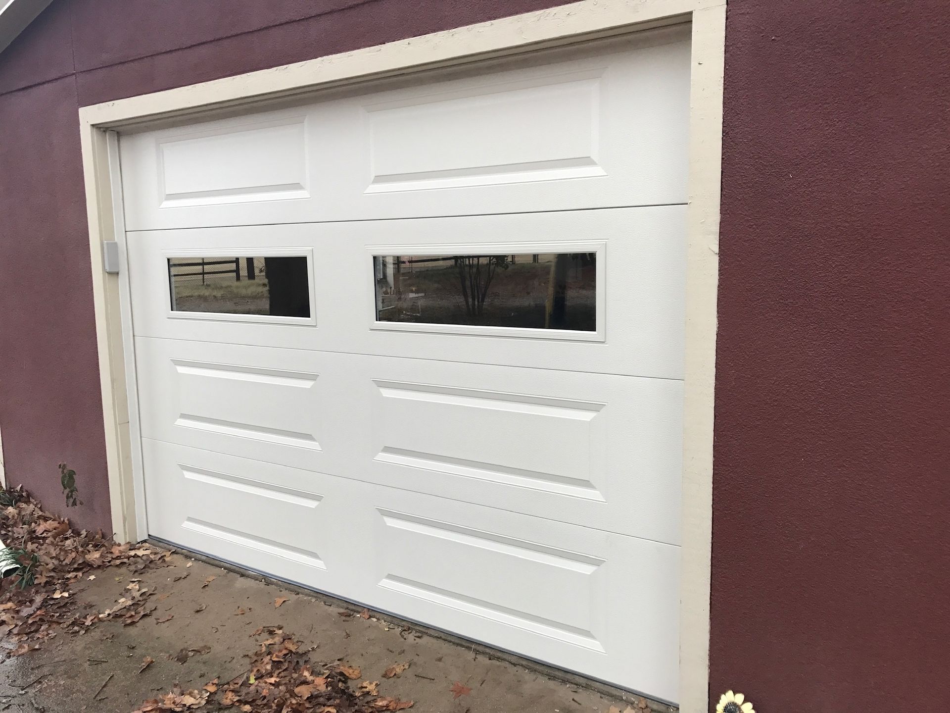 A white garage door with two windows on the side of a red building.
