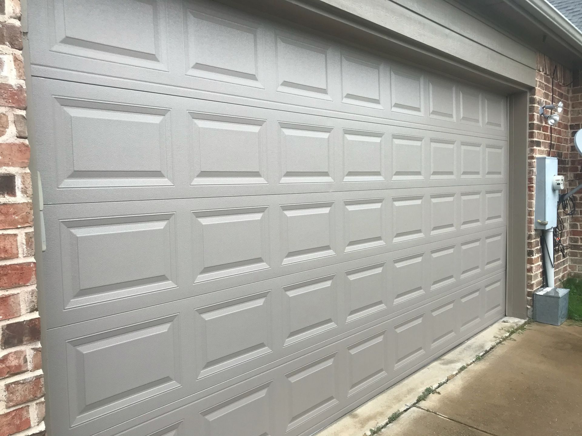 A gray garage door is sitting next to a brick building.