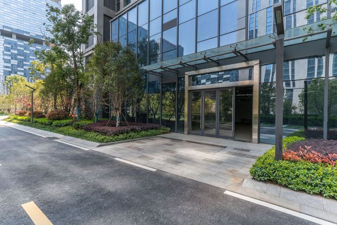 Modern office building entrance with glass doors, landscaped greenery, and a paved driveway
