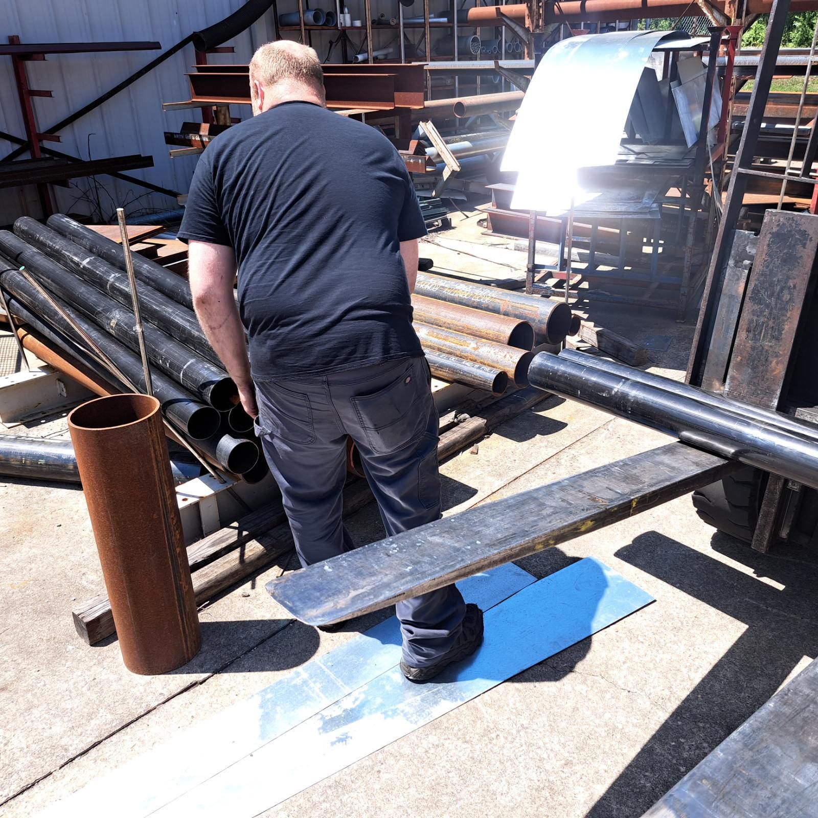 A man in a black shirt is standing in front of a pile of pipes