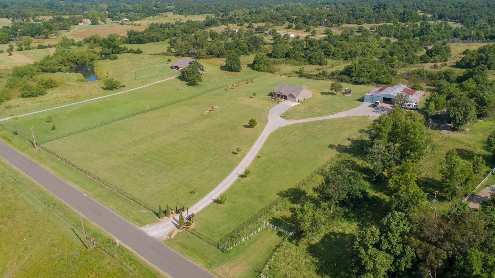 Aerial view of a rural property with a long driveway, green fields, scattered trees, and a house near the road