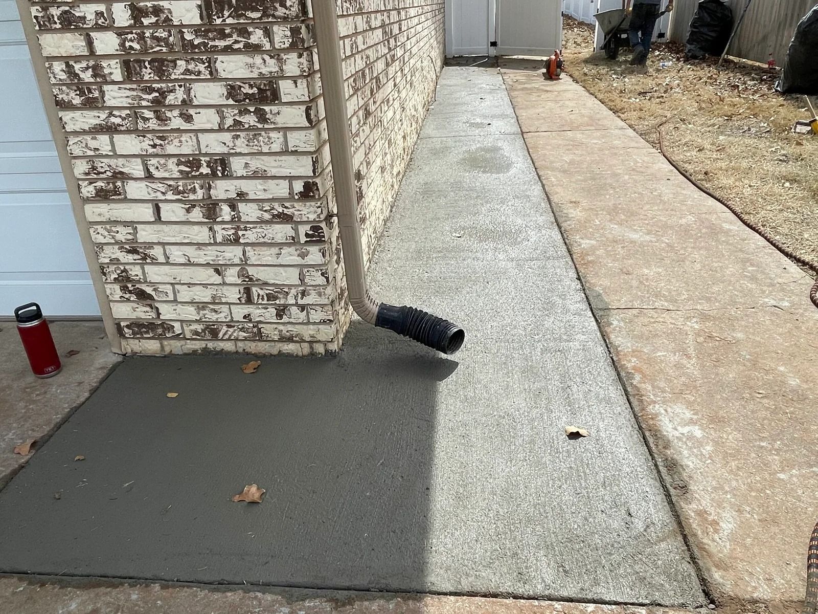 Cracked walkway beside brick house with loose black pipe and a red can near the wall
