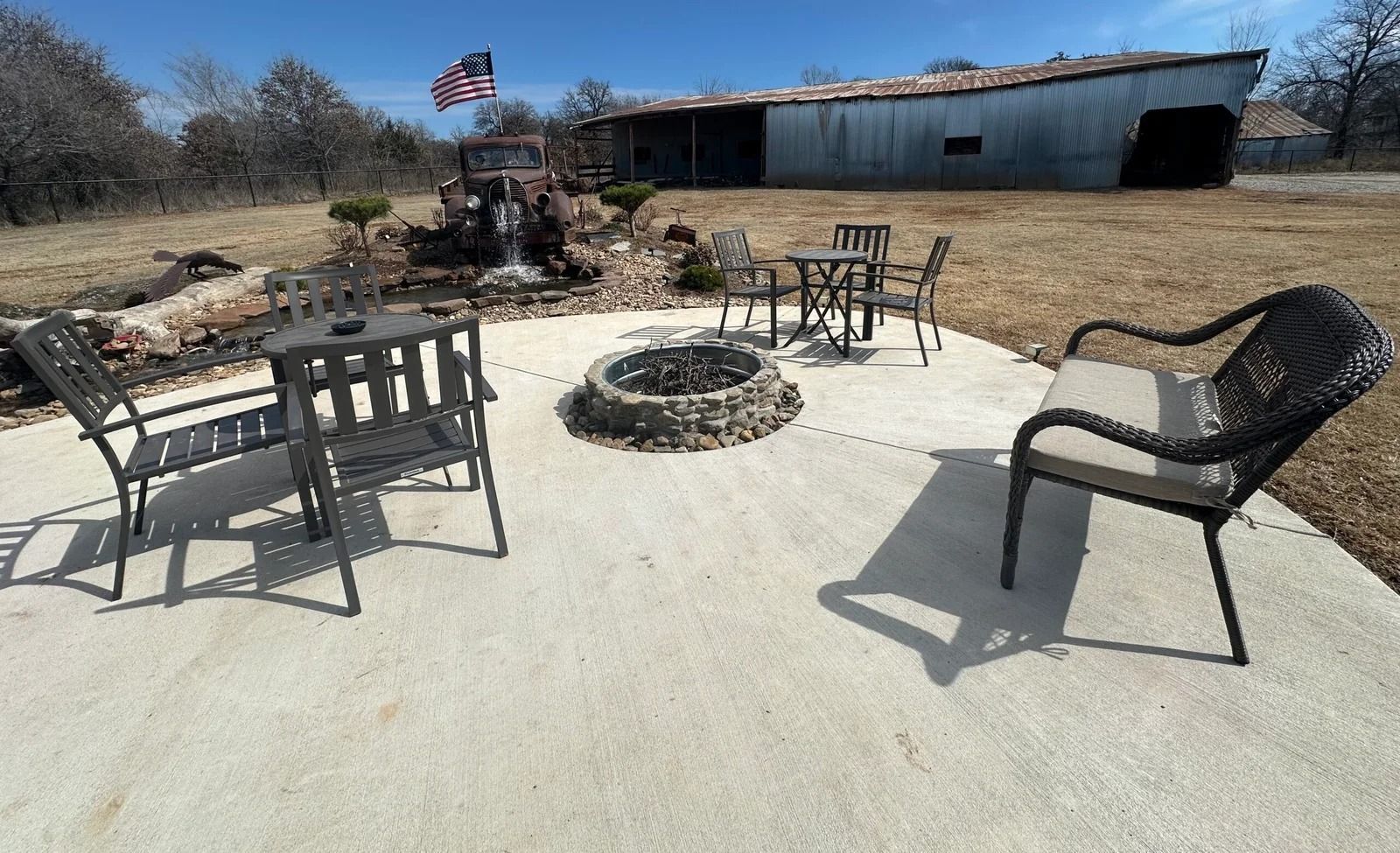Patio with metal chairs around a fire pit in a dry, open yard near a barn.