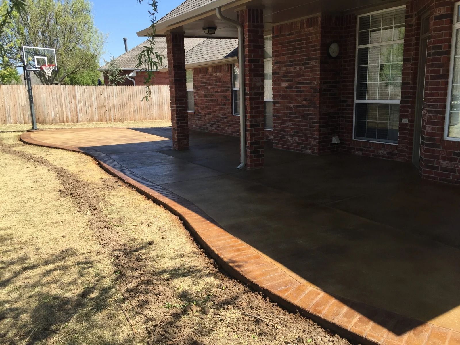 Brick house patio with covered porch and concrete slab beside a fenced backyard