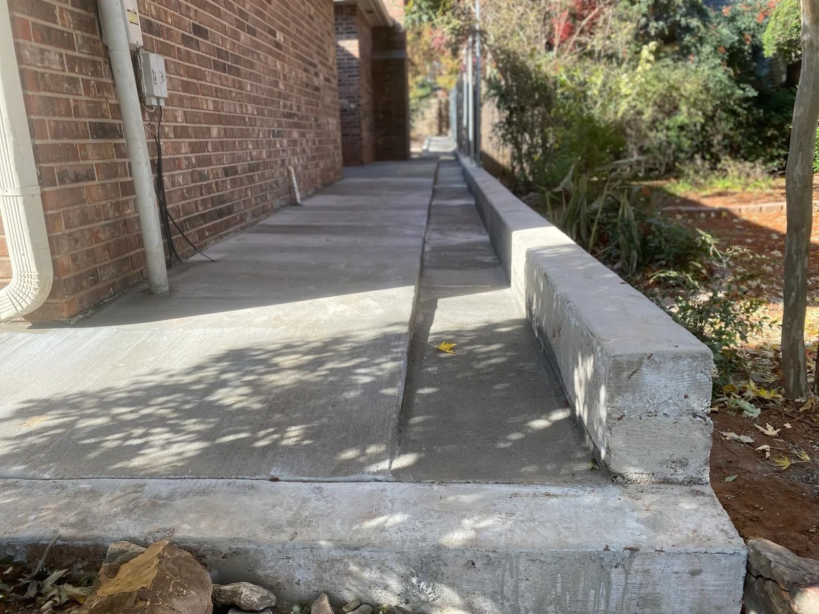 Concrete sidewalk beside a brick building, with a low curb and narrow accessible path leading ahead