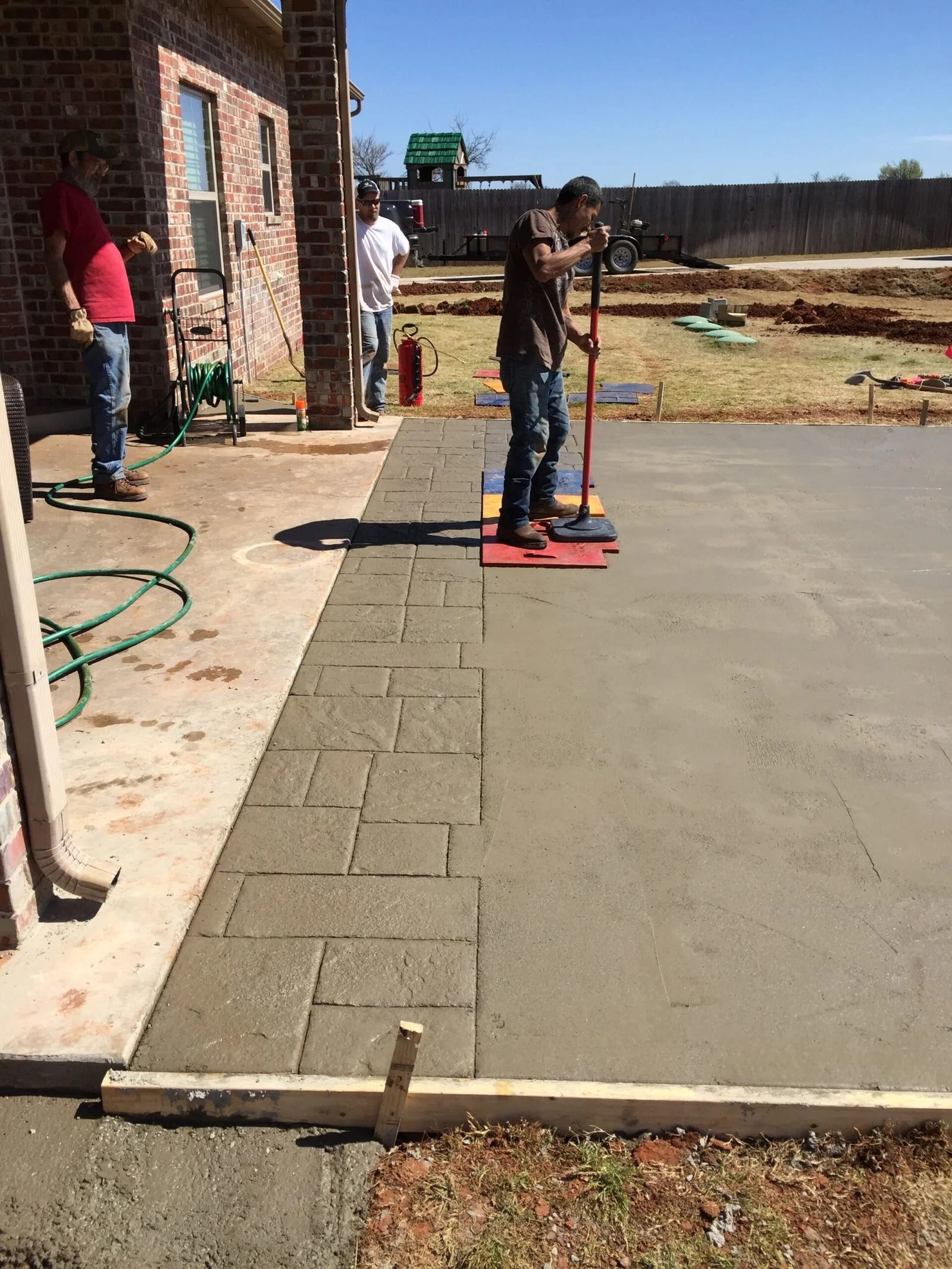 Worker smoothing fresh concrete beside a brick building on a construction site