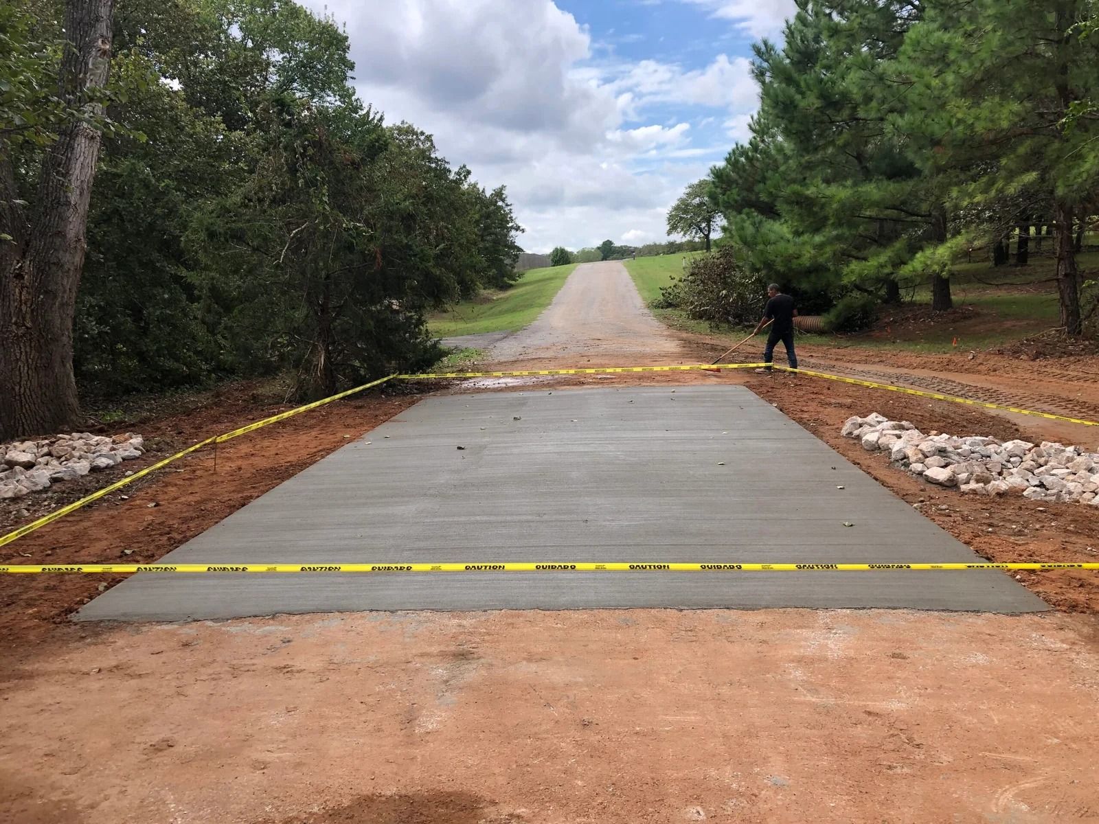 Concrete driveway crossing a dirt road in a wooded park, with yellow markings and a person standing to the right.