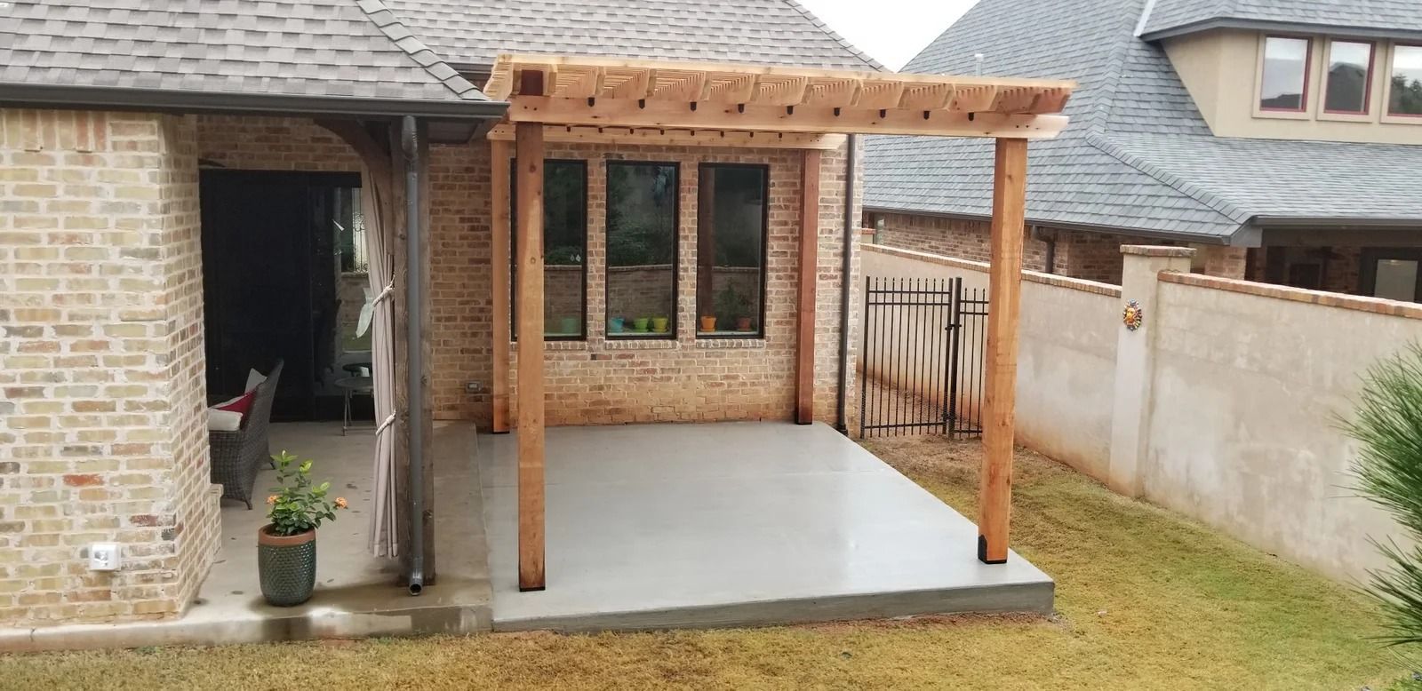 Back patio with covered wooden pergola, concrete slab, brick house wall, and grassy yard