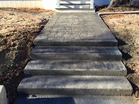 Concrete front steps leading to a paved walkway by a house entrance in a landscaped yard