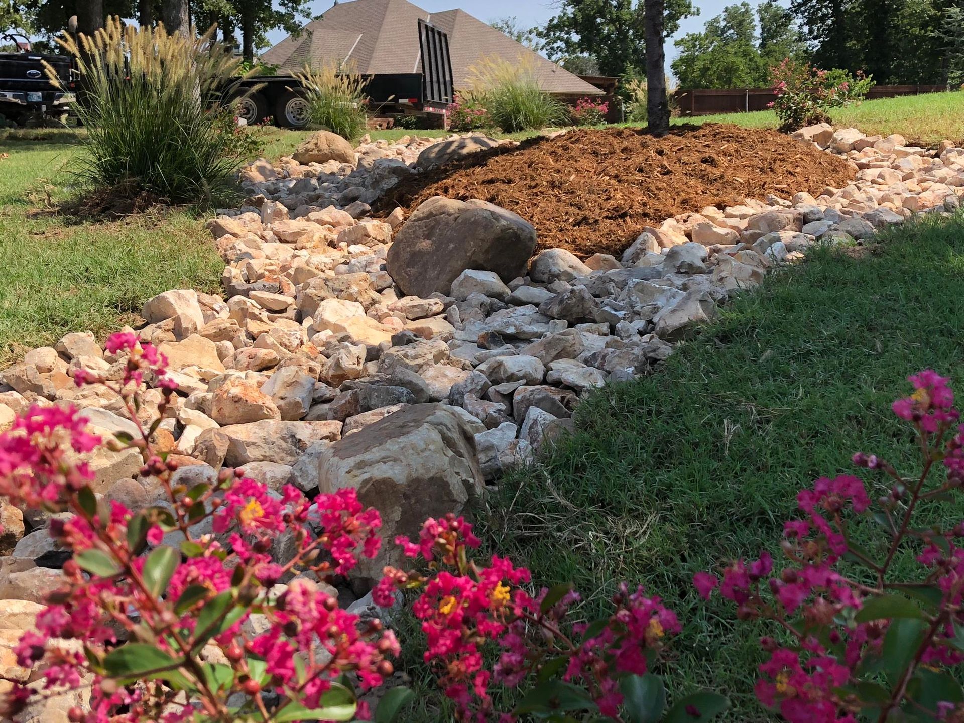 Rock garden with white stones, pink flowers, and a house in the background