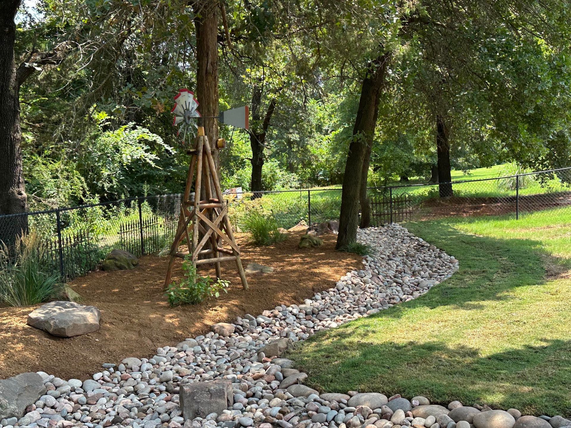 Wooden garden sculpture beside a curved border of gray rocks in a sunlit grassy park