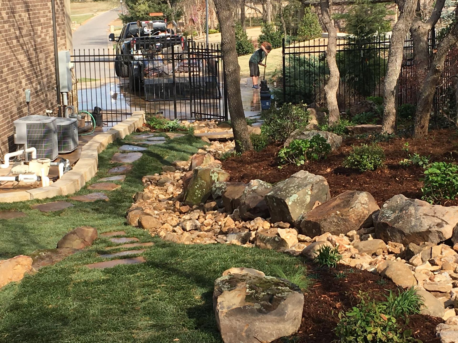 Stone-lined garden path with landscaped beds, rocks, and a black gate in the background