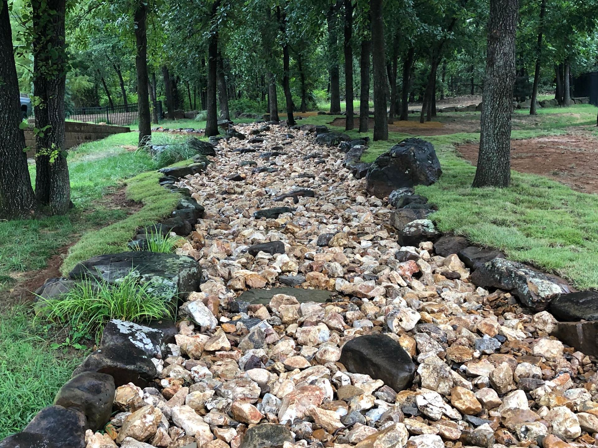Rock-filled drainage channel running through a forest with trees and green grass on both sides