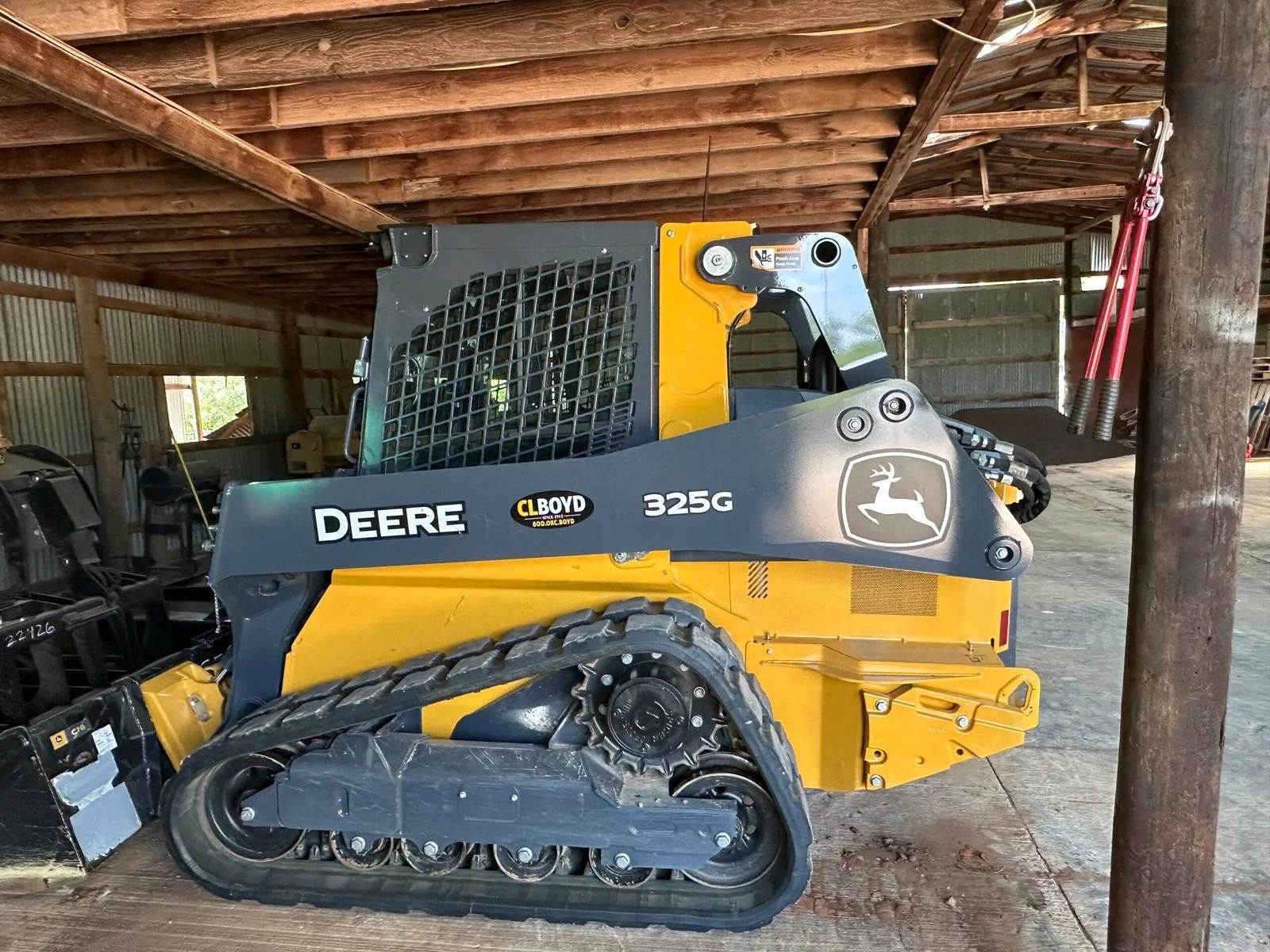 Yellow John Deere 325G compact track loader parked inside a wooden barn