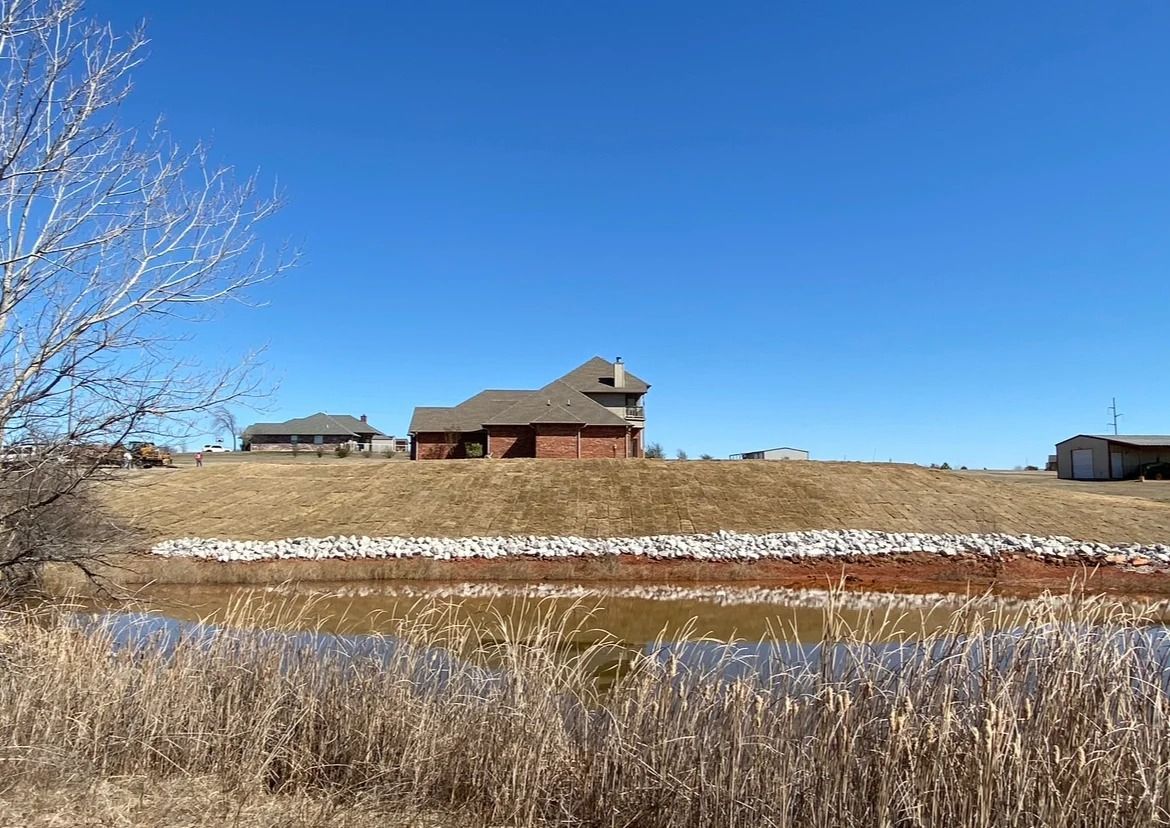 Rural barn on a snowy hillside under a clear blue sky, with a pond and dry grasses in the foreground