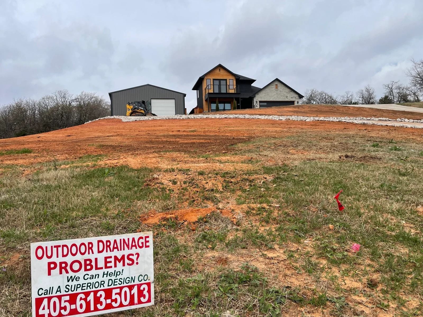 House on a bare hill with a drainage problem sign in the foreground