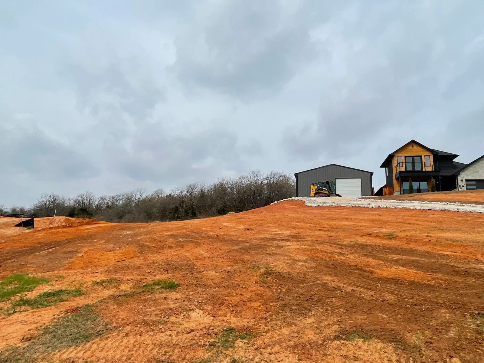 Orange dirt lot with two houses on a hill under a cloudy sky
