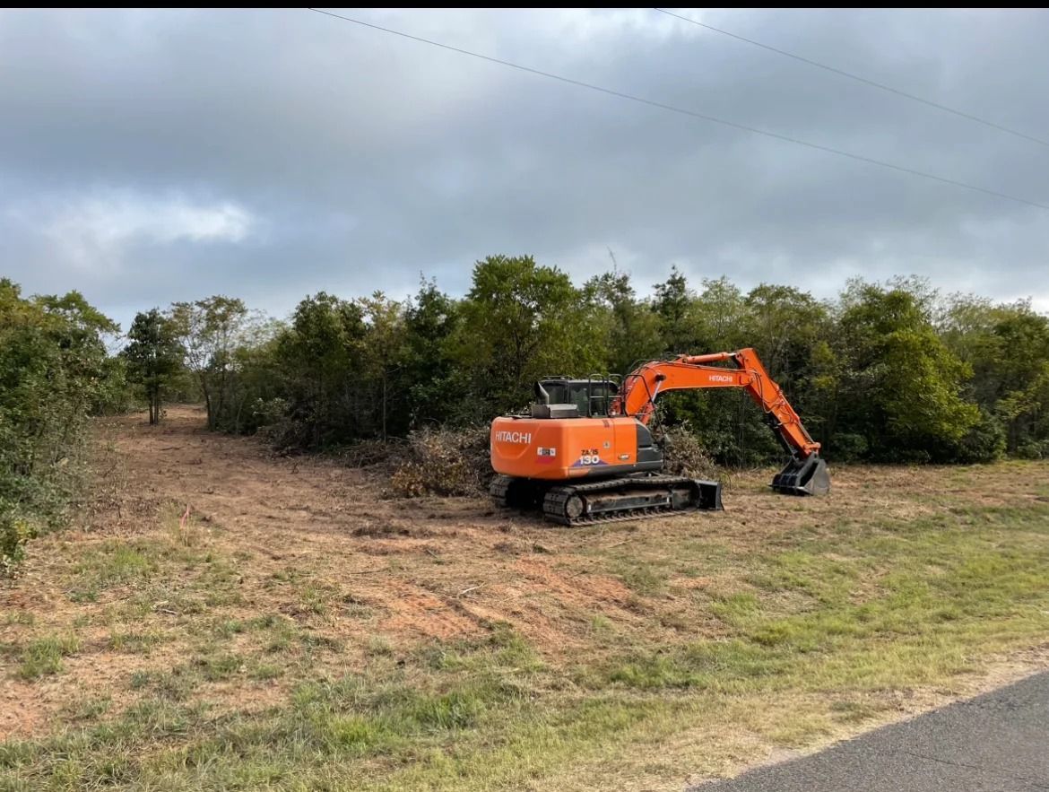 Orange excavator on a grassy roadside clearing under cloudy skies