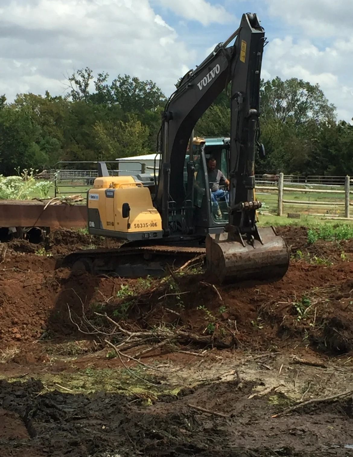 Yellow excavator clearing muddy ground in a fenced outdoor area