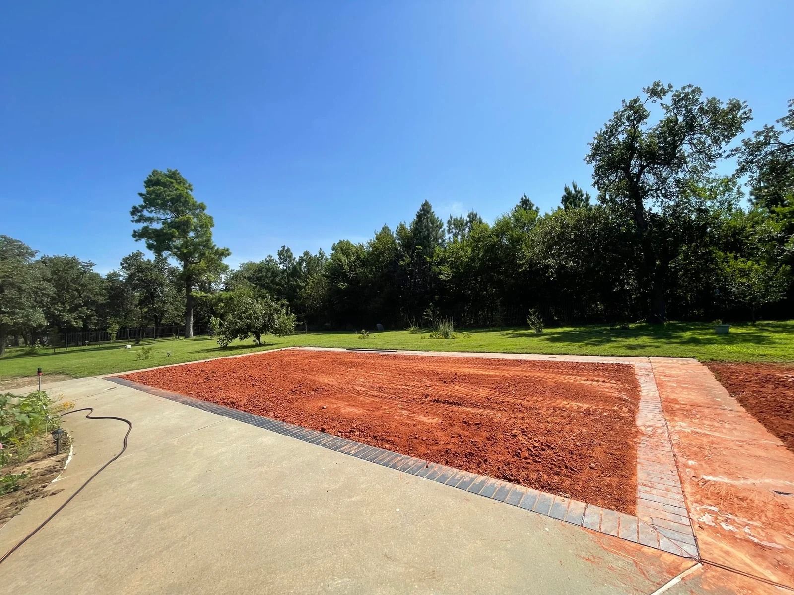 Curved walkway beside a red mulch bed in a sunny park with trees and blue sky