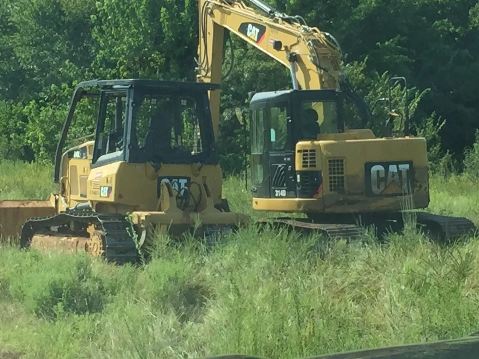 Yellow CAT excavator in tall grass at a wooded construction site