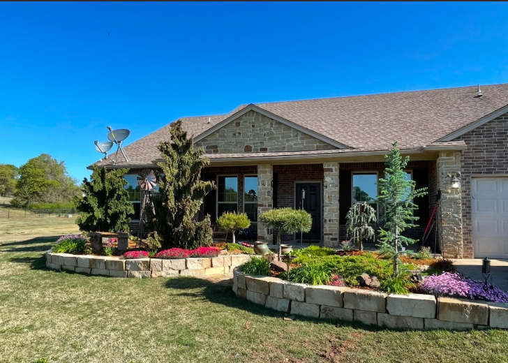 Brick suburban house with landscaped front garden, stone edging, and bright blue sky