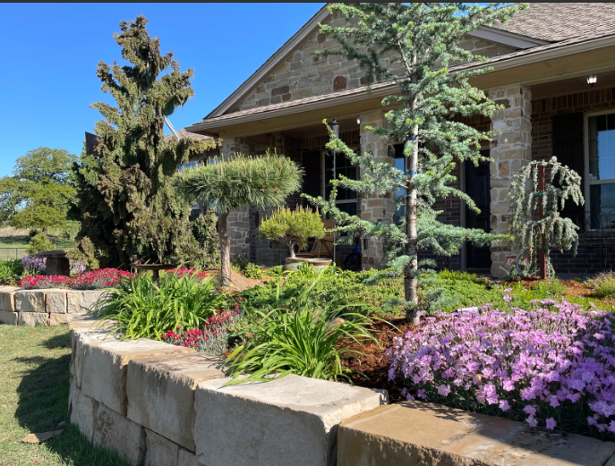 Stone house with a landscaped garden of purple flowers, red blooms, and manicured shrubs under a blue sky