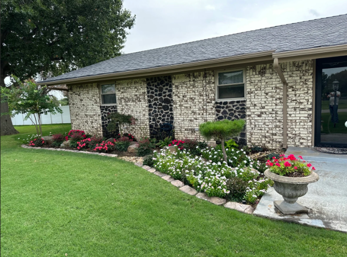 Brick house with manicured lawn, flower beds, and a decorative planter by the entrance