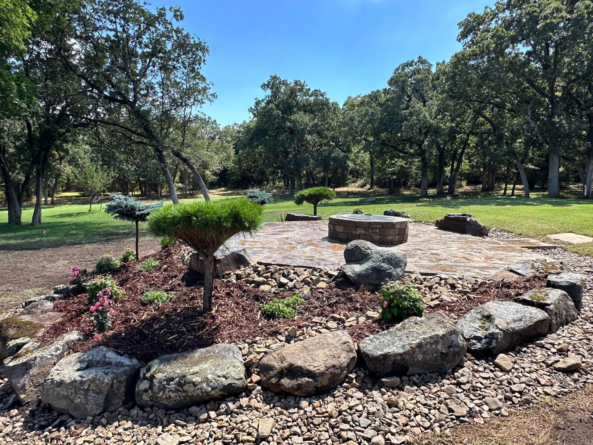 Rock garden with stones and small shrubs in a sunny park with trees and grass.