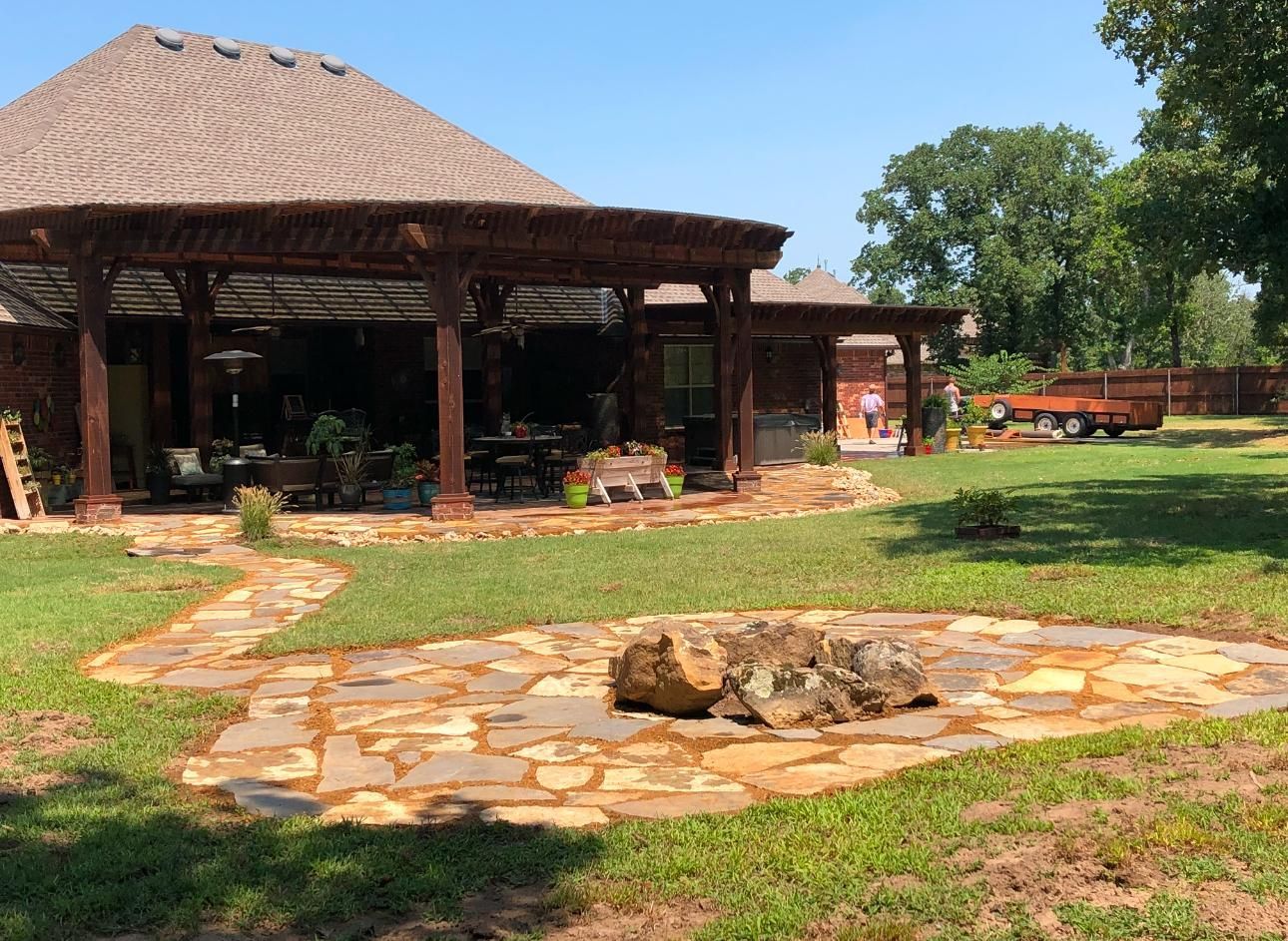 Rustic lodge with thatched roof, stone patio, and fire pit in a sunny grassy setting