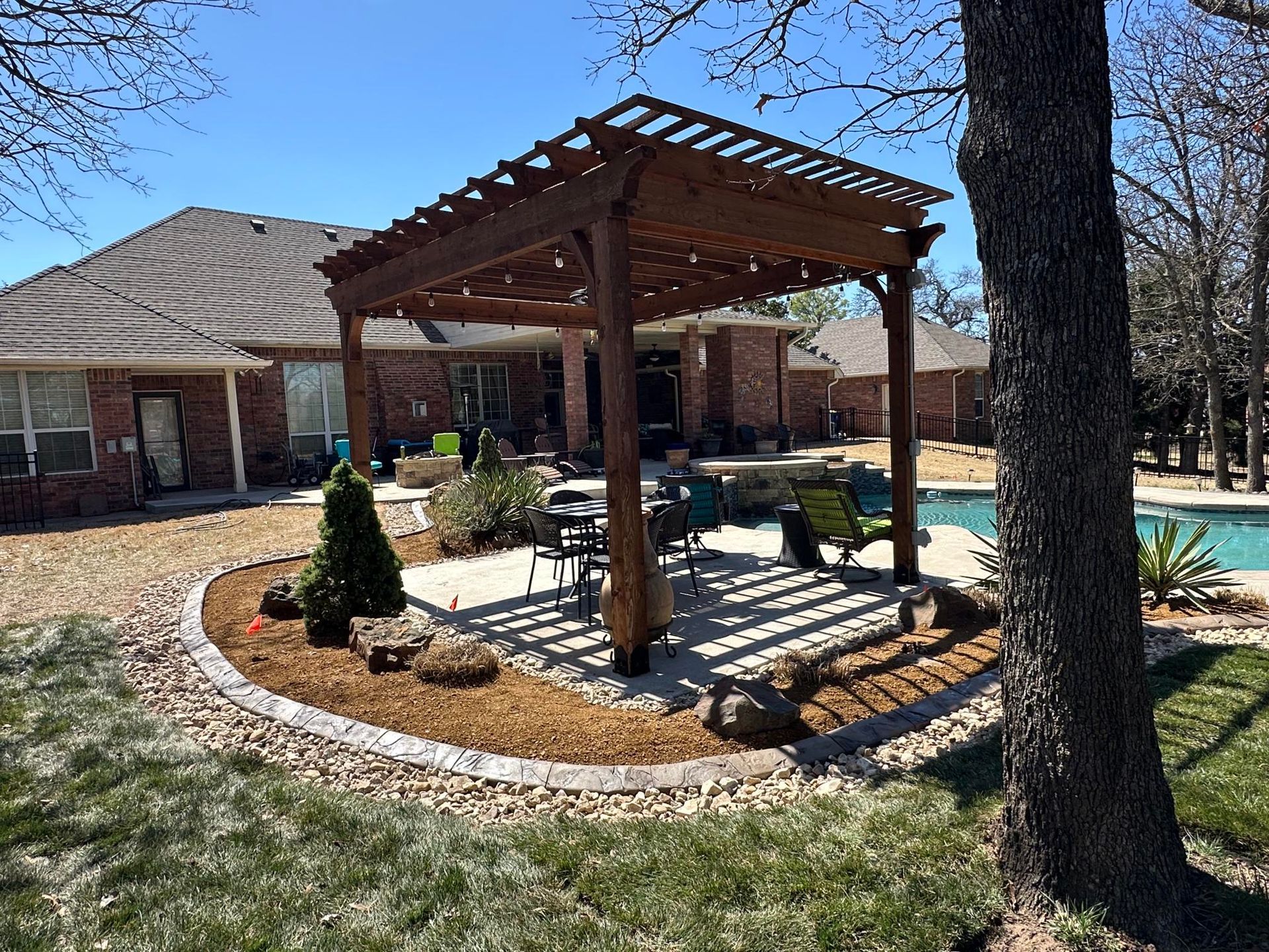 Backyard patio with wooden pergola, outdoor seating, and pool beside a brick house