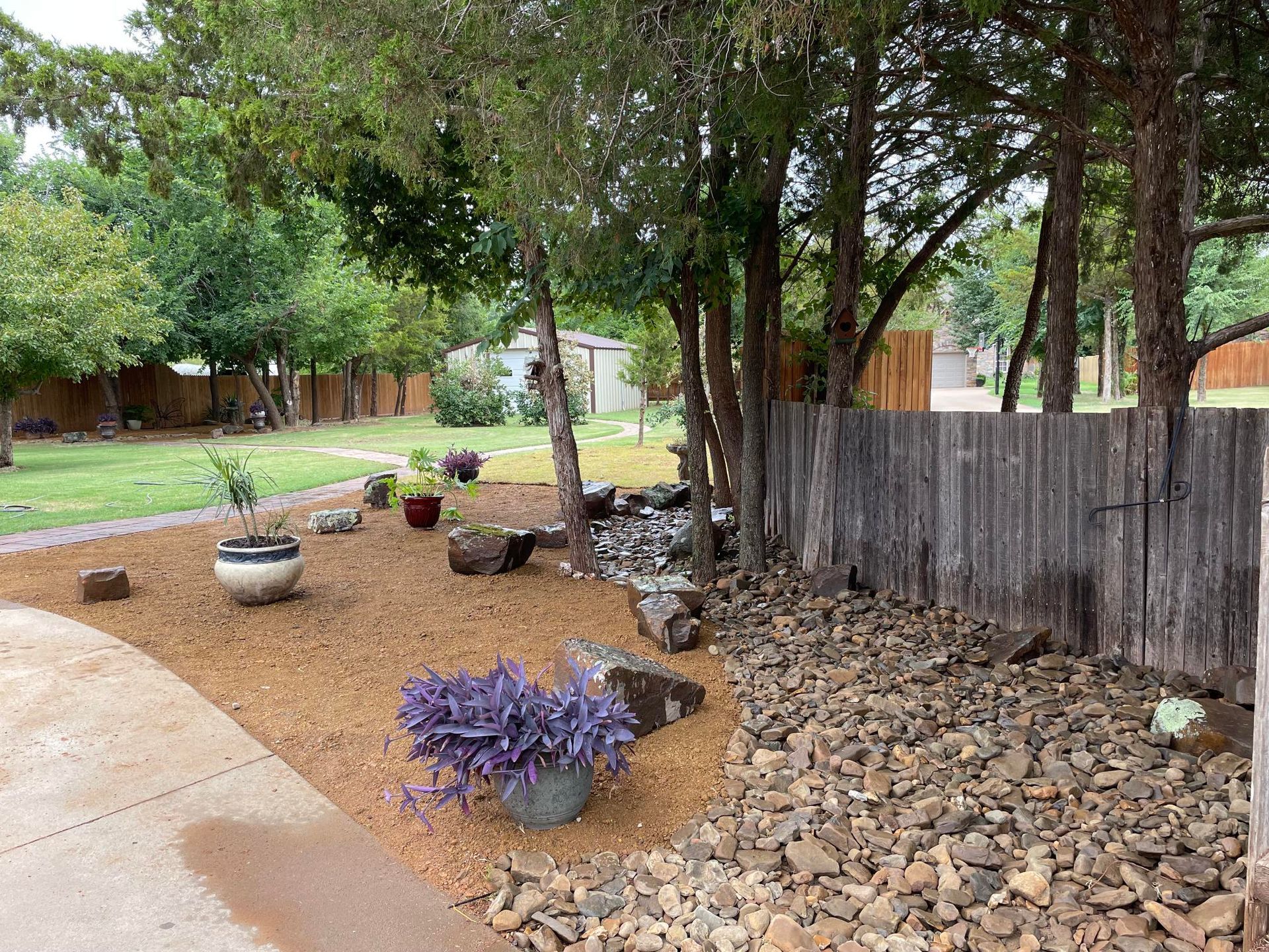 Stone retaining wall beside a sloped sidewalk next to a brick building and dirt landscaping.