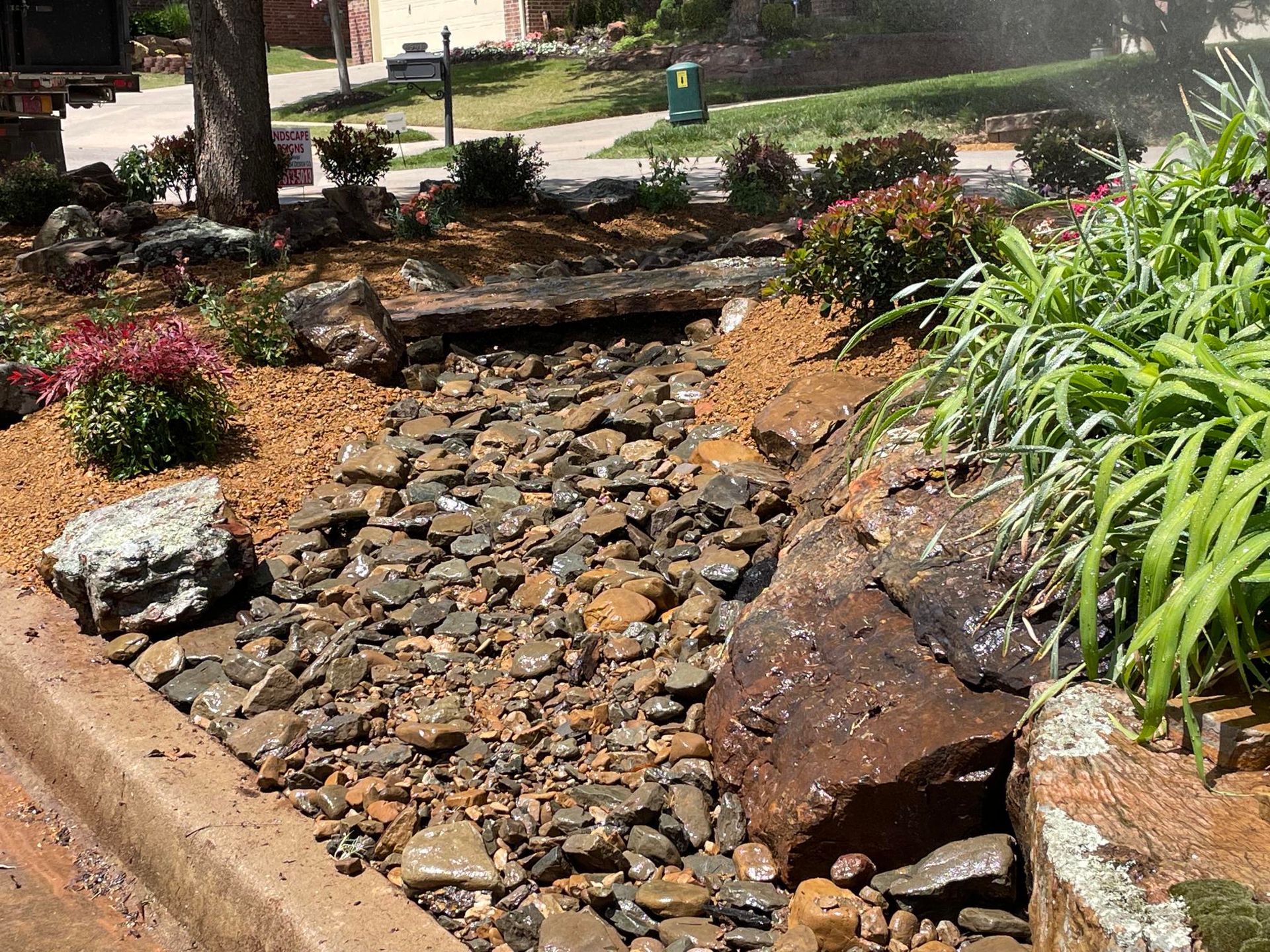 Rock garden dry creek bed with stones, rocks, and green plants in a landscaped yard
