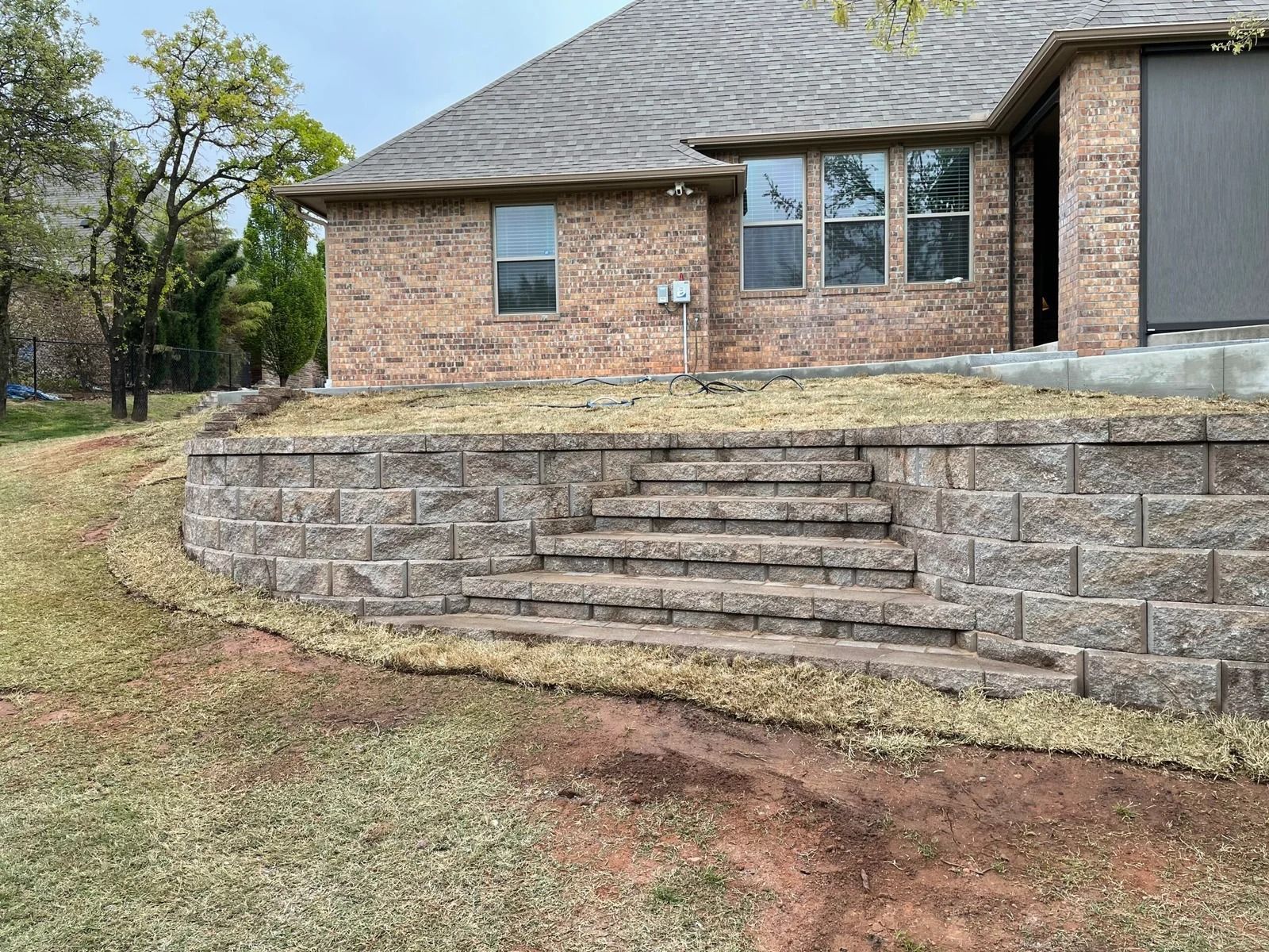 Brick house with stone retaining wall and steps in a grassy yard