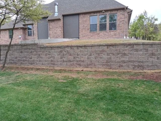 Brick house behind a stone retaining wall with a grassy yard in front