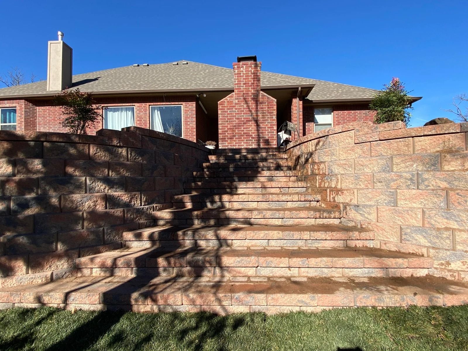 Brick house behind stone retaining walls and steps under a clear blue sky