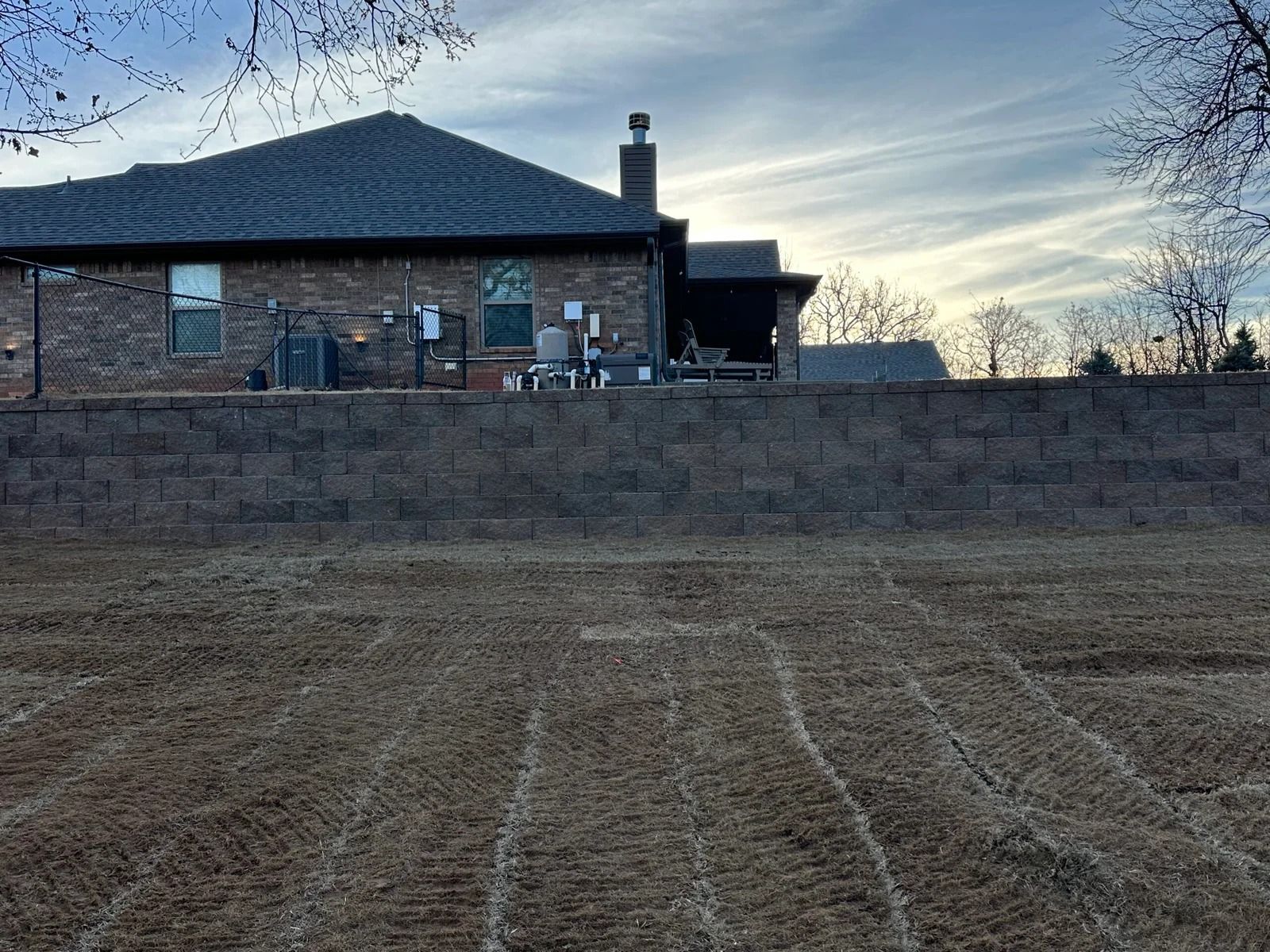 Backyard lawn with a brick house and tall stone wall at dusk