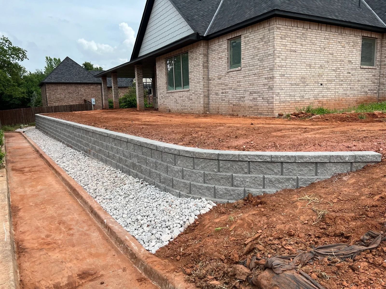 Stone retaining wall along a house driveway with white gravel and red dirt landscaping