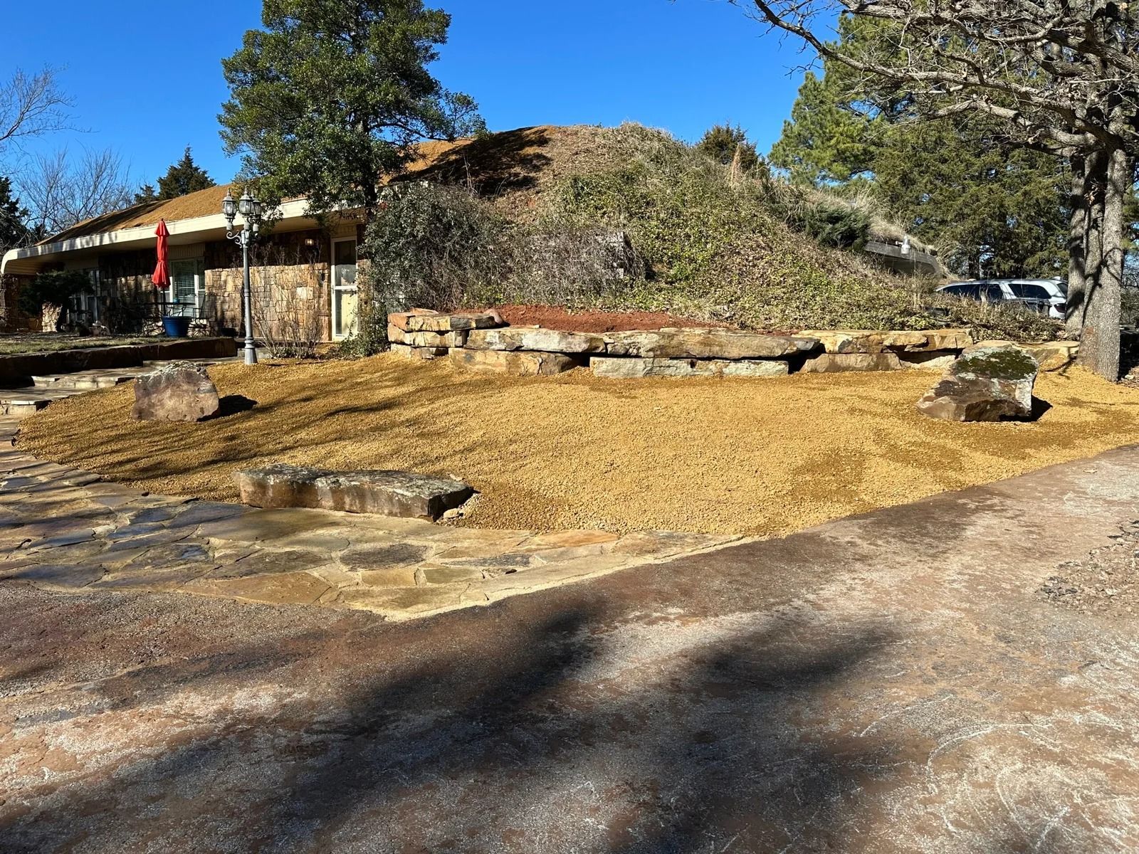 Dry, landscaped yard with a large rock feature, mulch, and a house in the background.