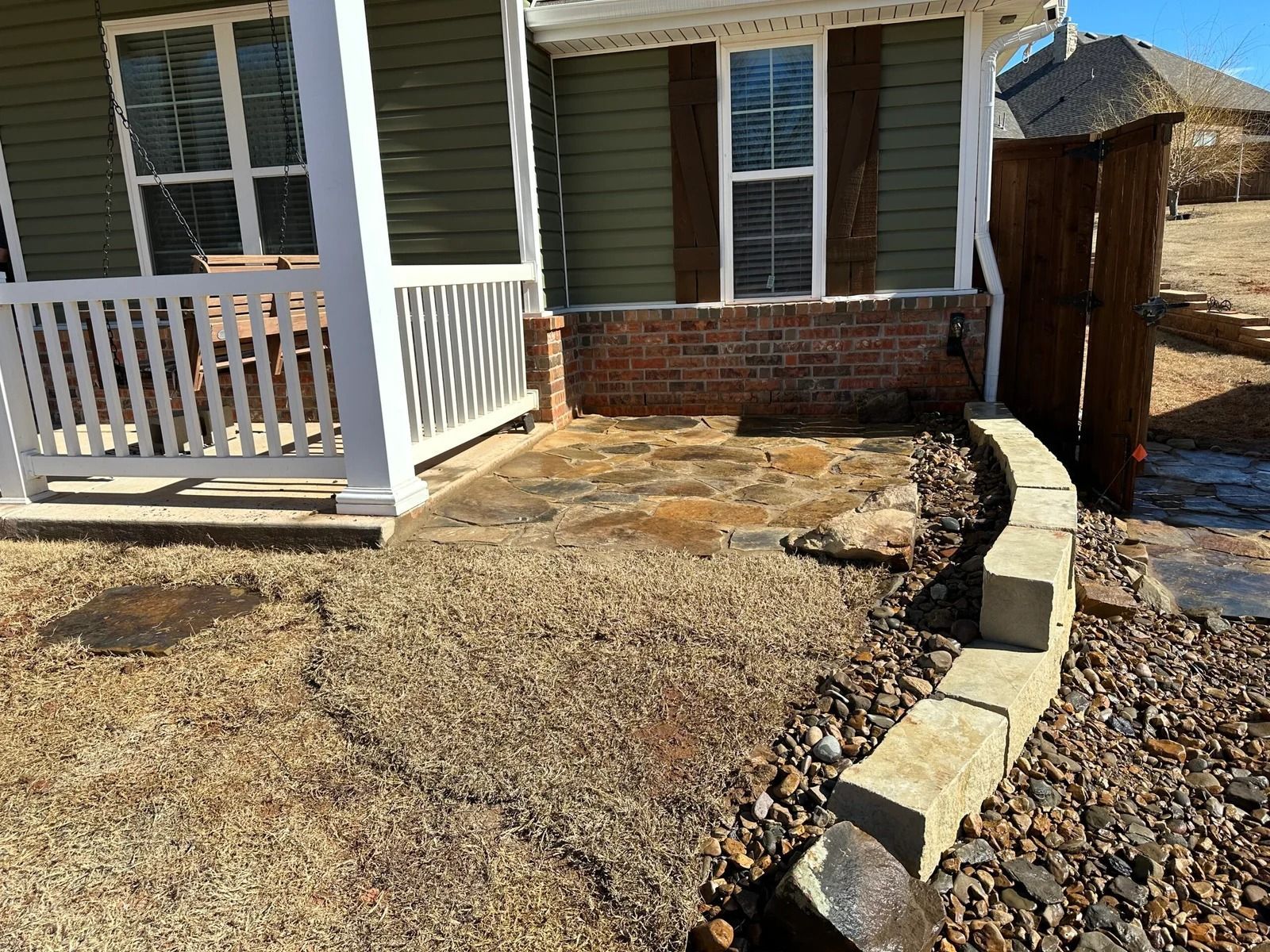 Front porch with white railing, brick steps, and a stone-bordered gravel path in a residential yard