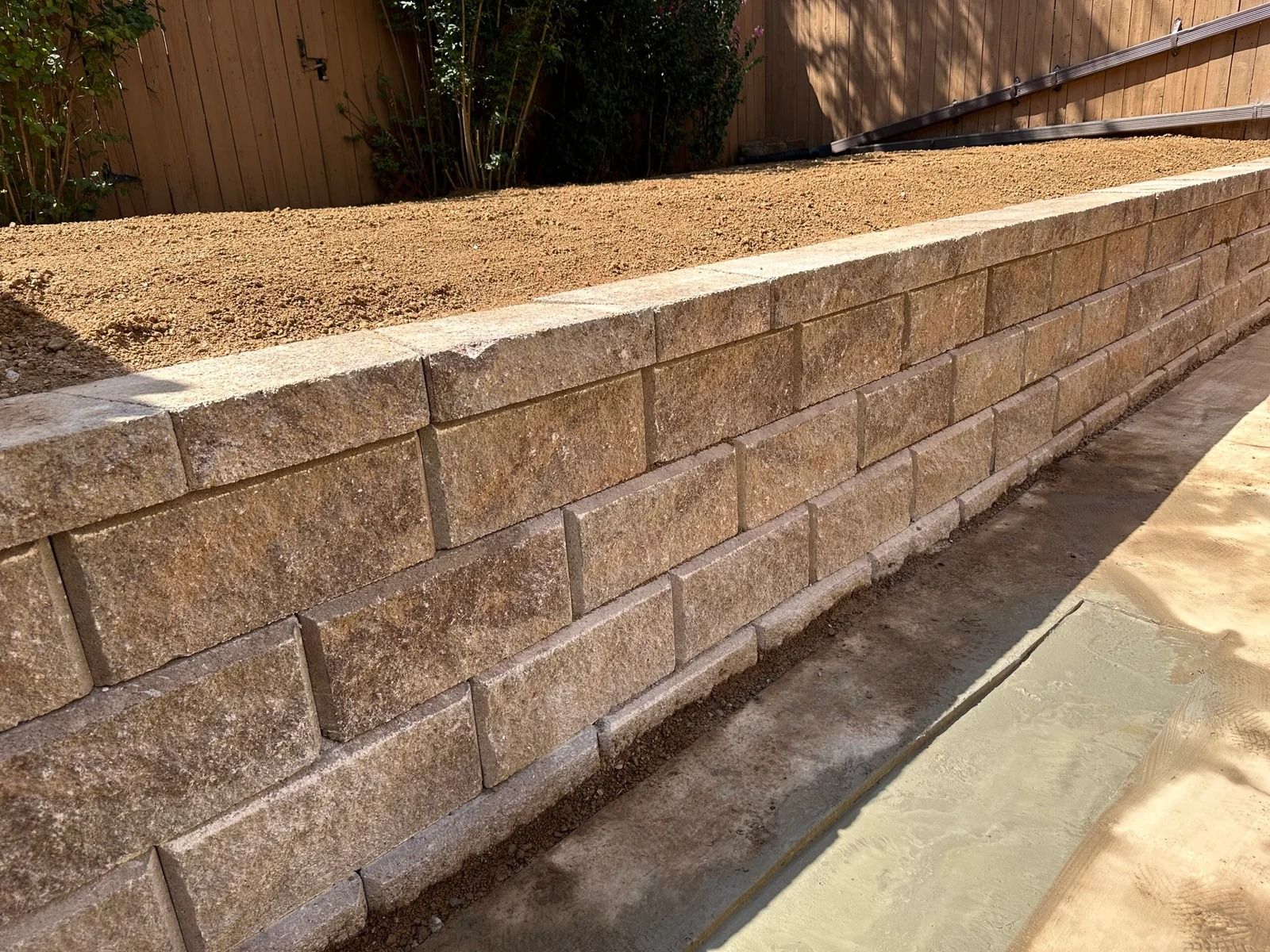 Tan brick retaining wall with gravel top along a sloped walkway in daylight