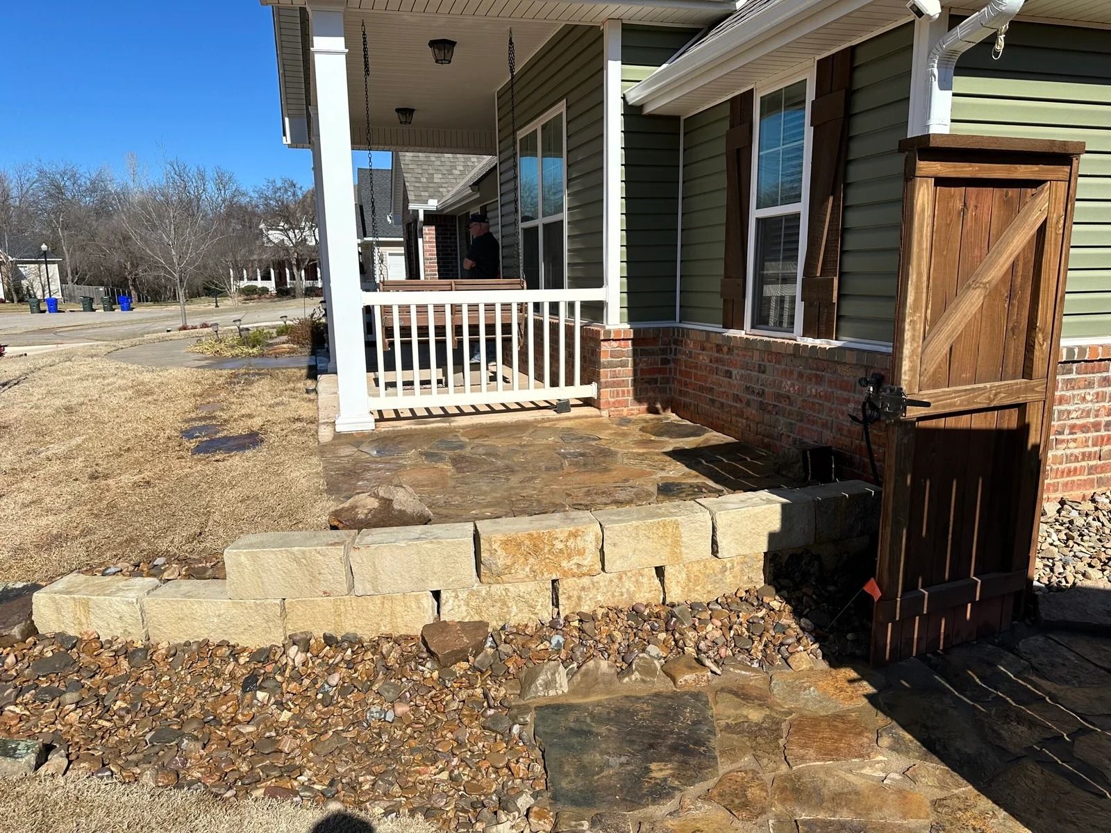 Front porch with brick house, stone steps, white railing, and wooden gate beside a driveway
