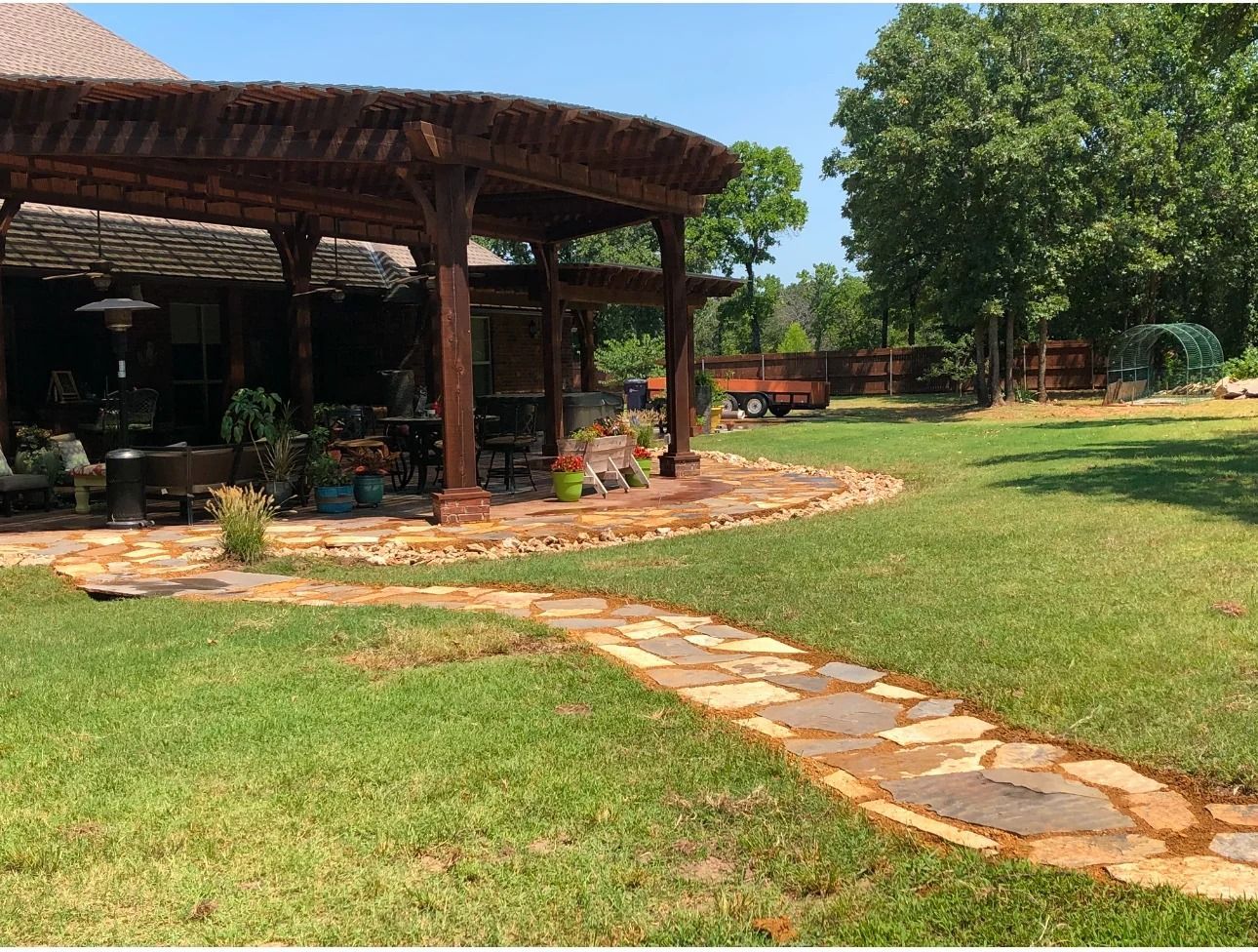Garden with stone path leading to a shaded wooden pavilion and trees on a sunny day