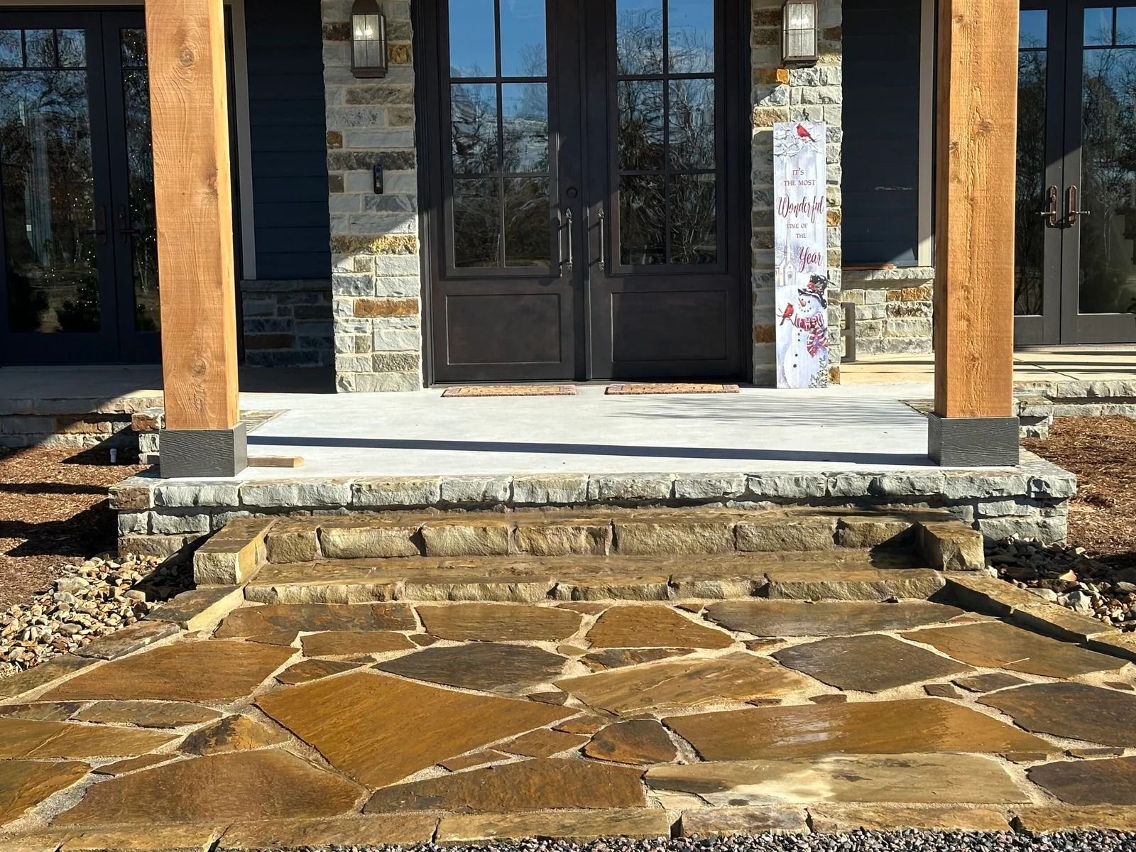 Stone front porch with wooden columns, double glass doors, and a patterned stone walkway