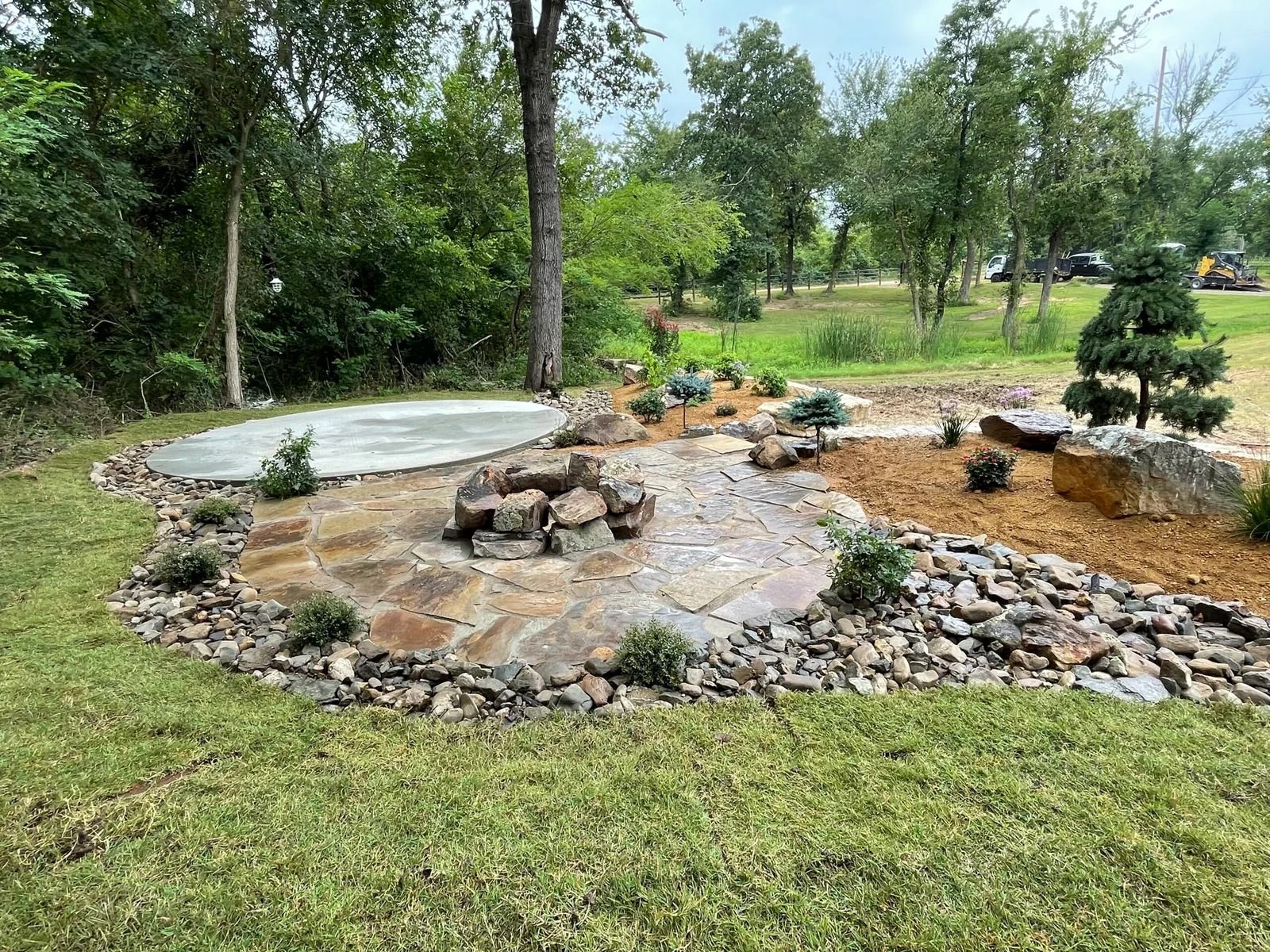 Rock garden with stones, small shrubs, and a curved concrete path in a grassy park.