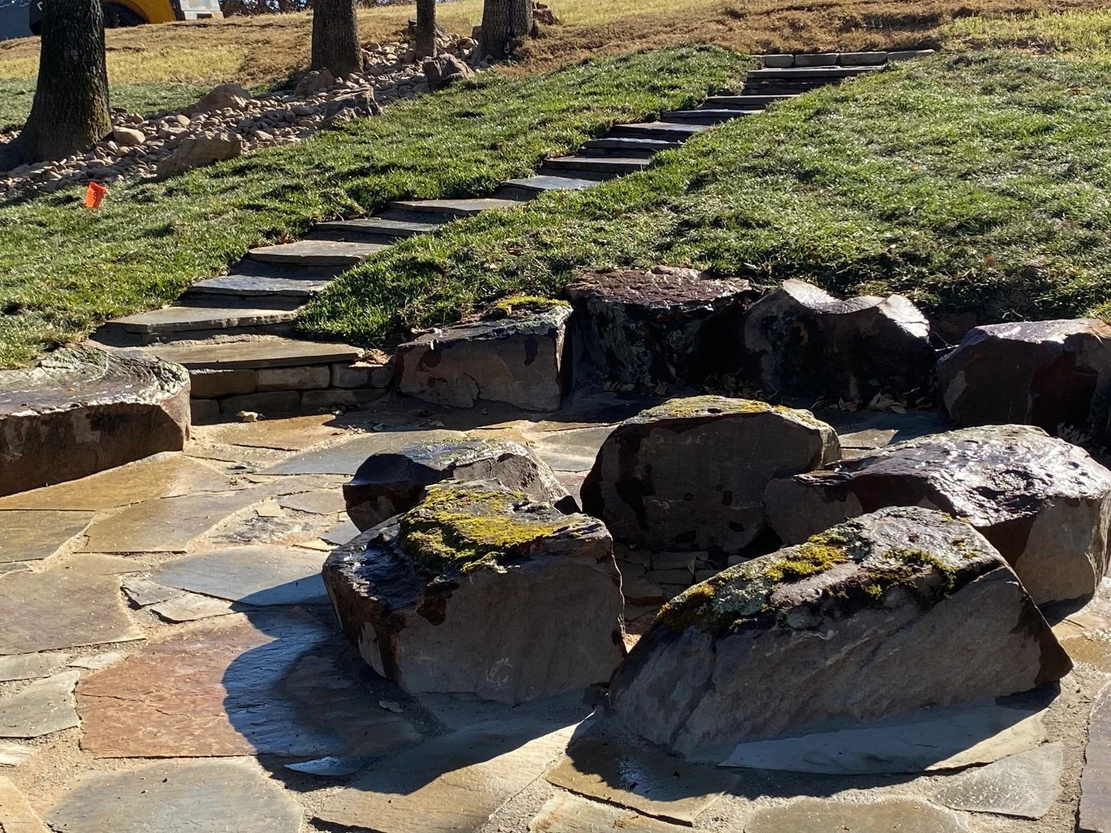 Stone-lined spring with clear water and mossy rocks in a grassy park, with a stepping-stone path nearby