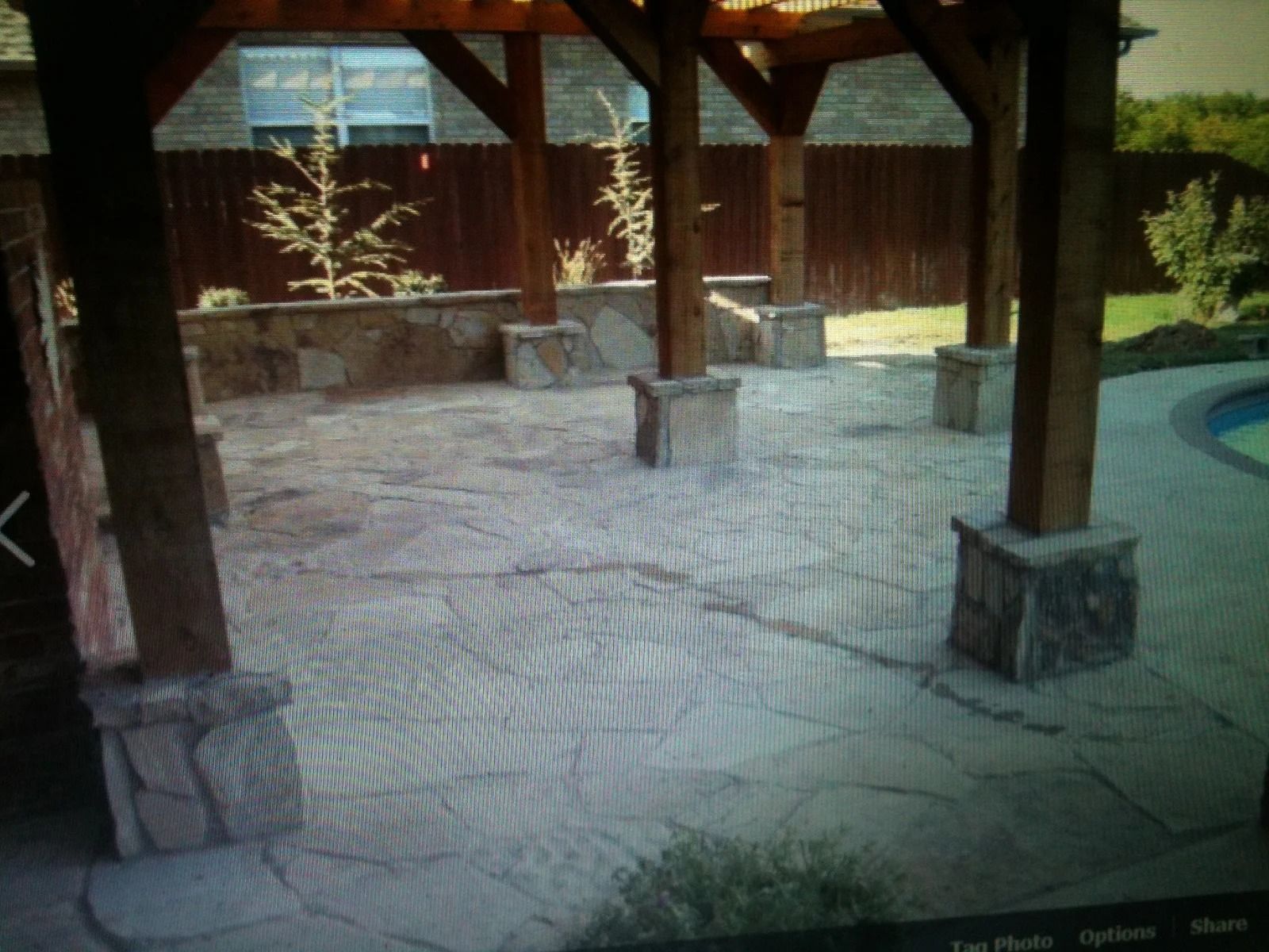 Covered stone patio with wooden posts, built-in benches, and sunny garden views beyond the railing