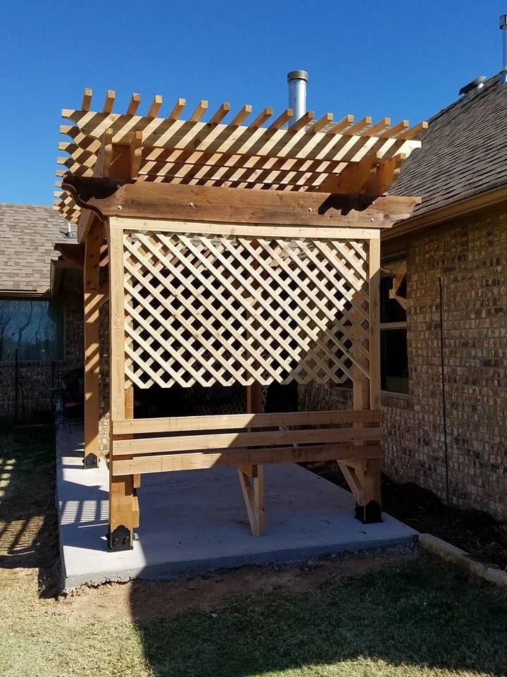 Wooden pergola and lattice screen in a backyard beside a brick house, under a clear blue sky