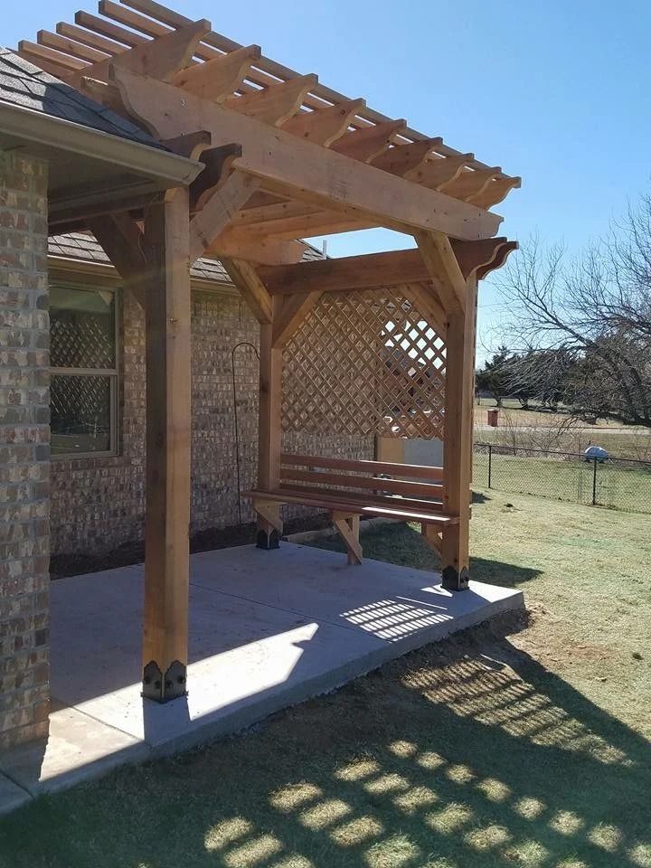 Wooden pergola-covered porch beside a house, with lattice wall and bench in a sunny yard.